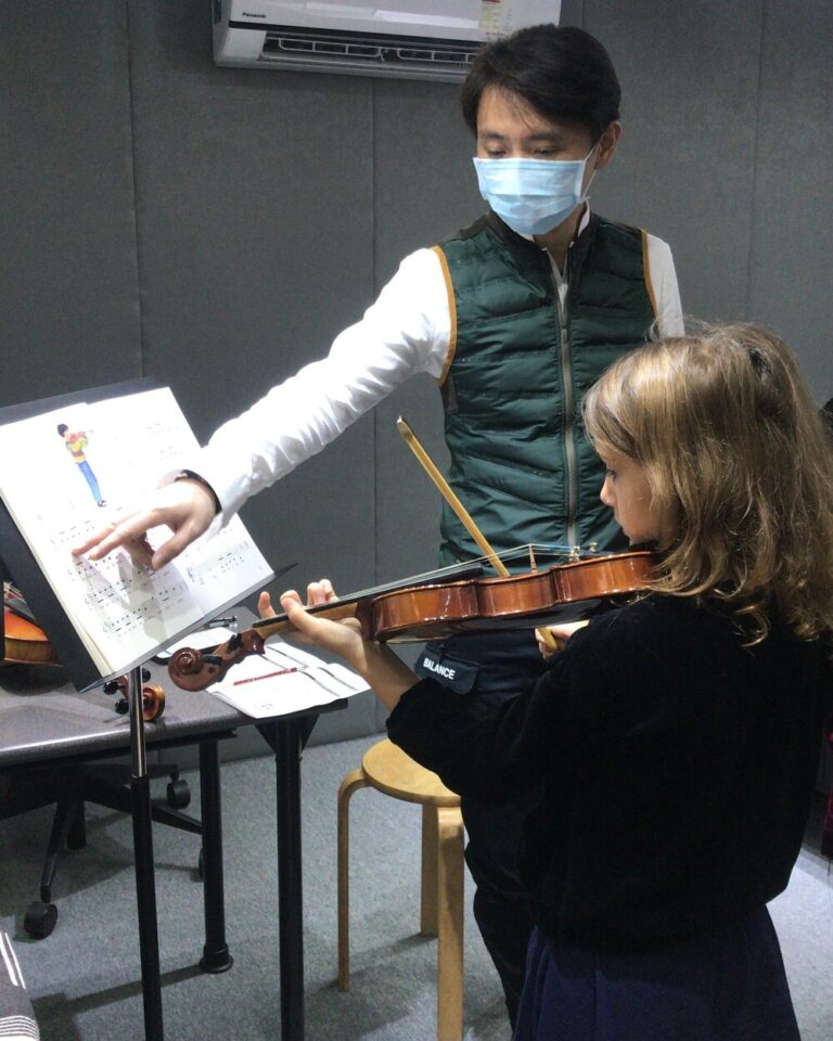 Stephen is giving a 1-on-1 violin lesson, pointing to the sheet music on a stand for a young student.