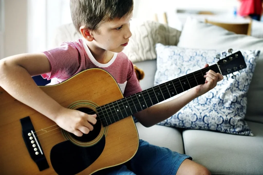 A little boy is playing guitar in his house.